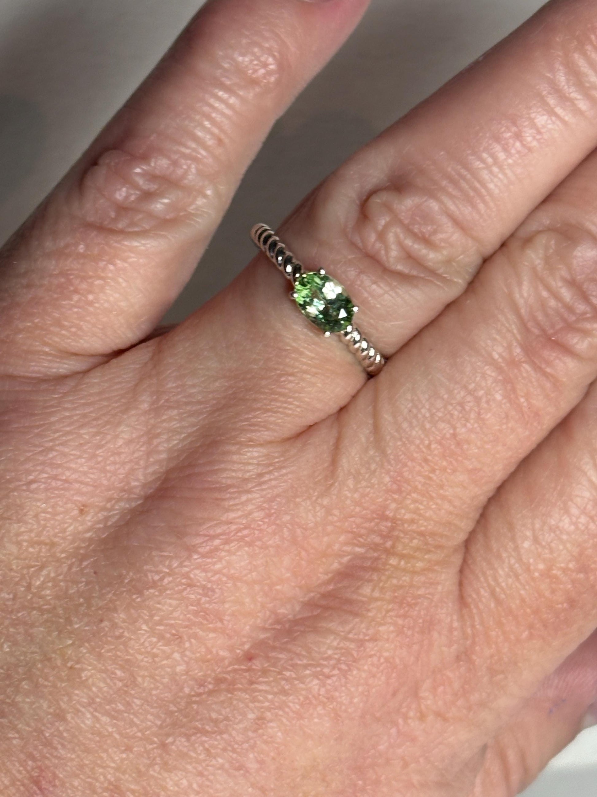 Sterling silver ring with an oval green tourmaline in an east-west setting on a rope band.