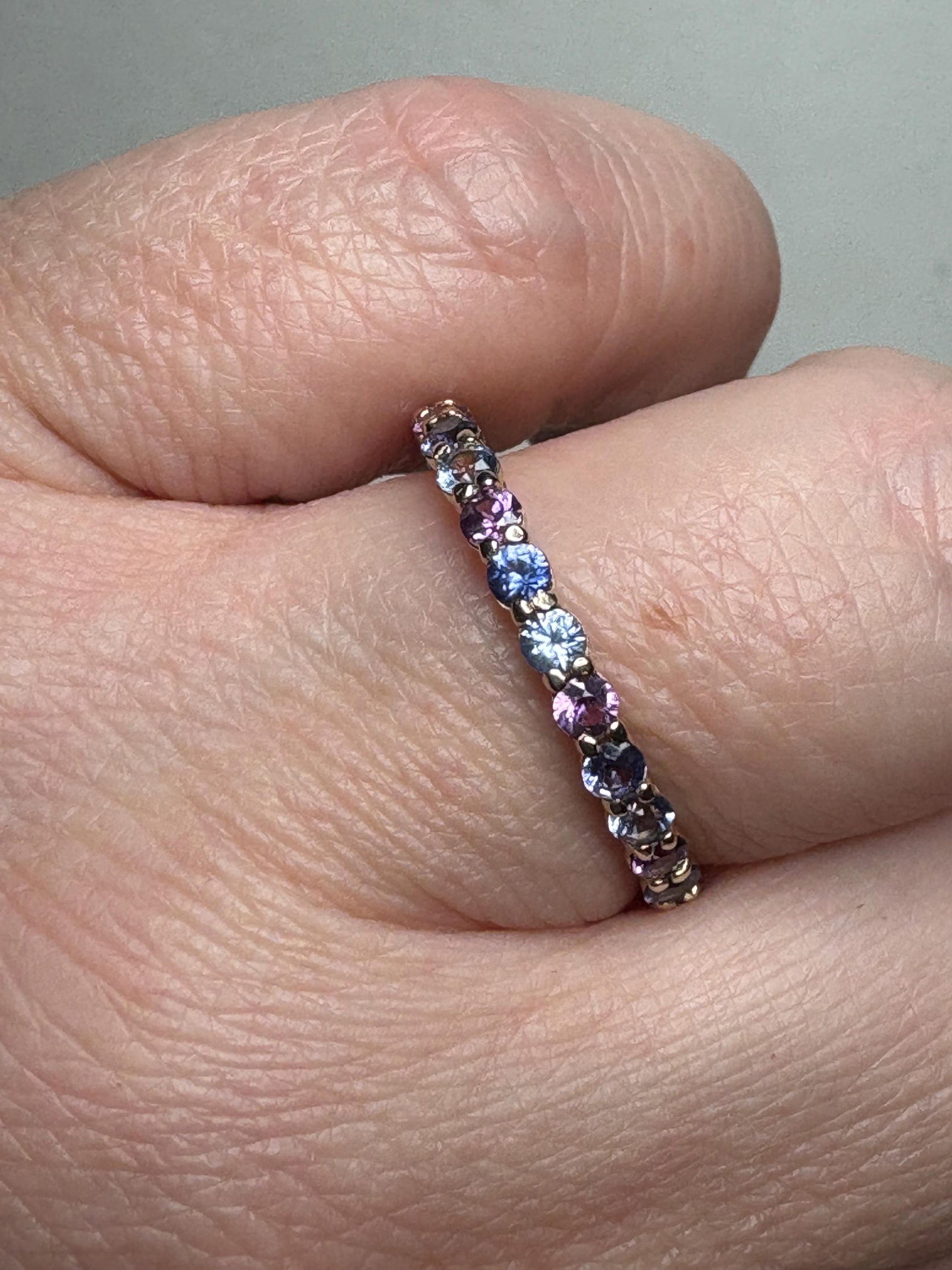 A 14k gold band ring with a row of multi-colored sapphires.