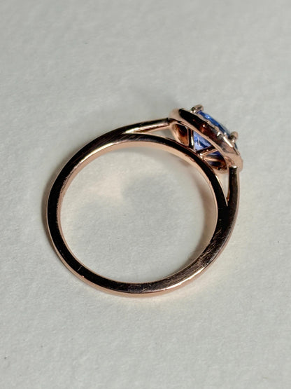 A rose gold ring with a tanzanite center stone and diamond halo.