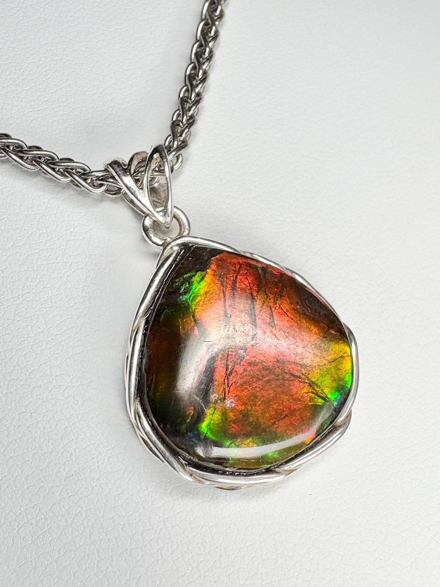 Sterling silver pendant necklace with a pear-shaped ammolite gemstone featuring red and green colors.