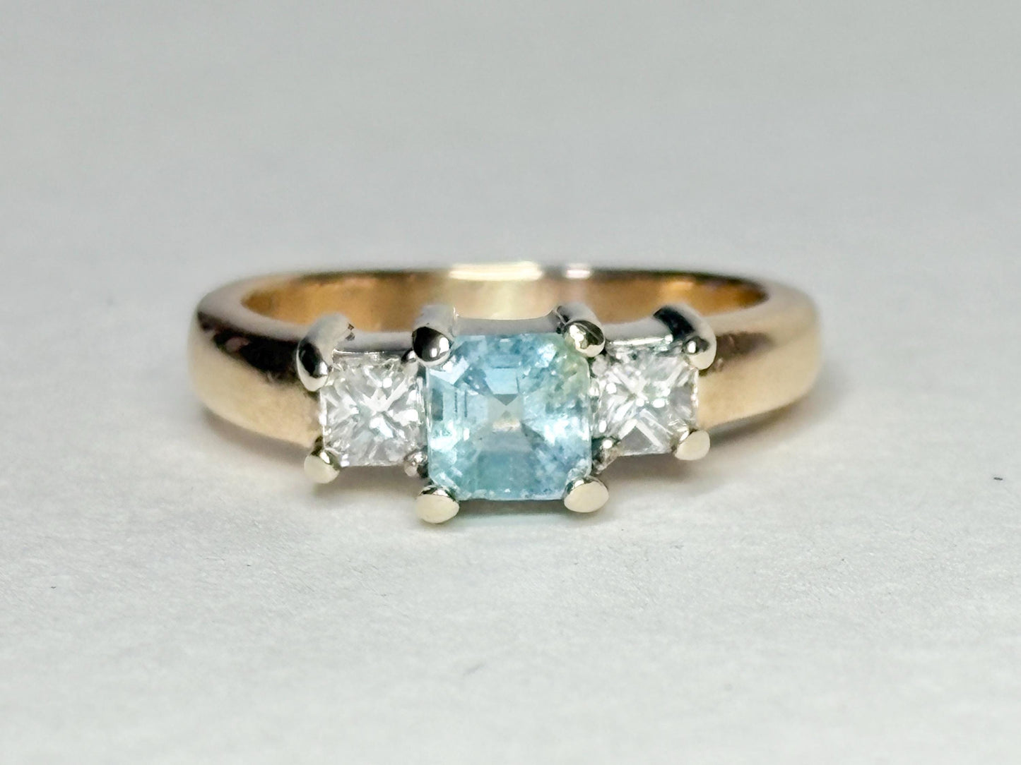Gold ring with a blue asscher cut tourmaline and two princess cut diamonds.