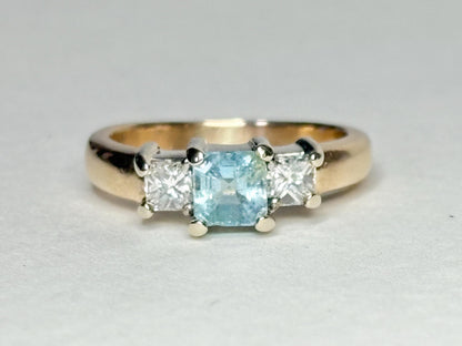 Gold ring with a blue asscher cut tourmaline and two princess cut diamonds.