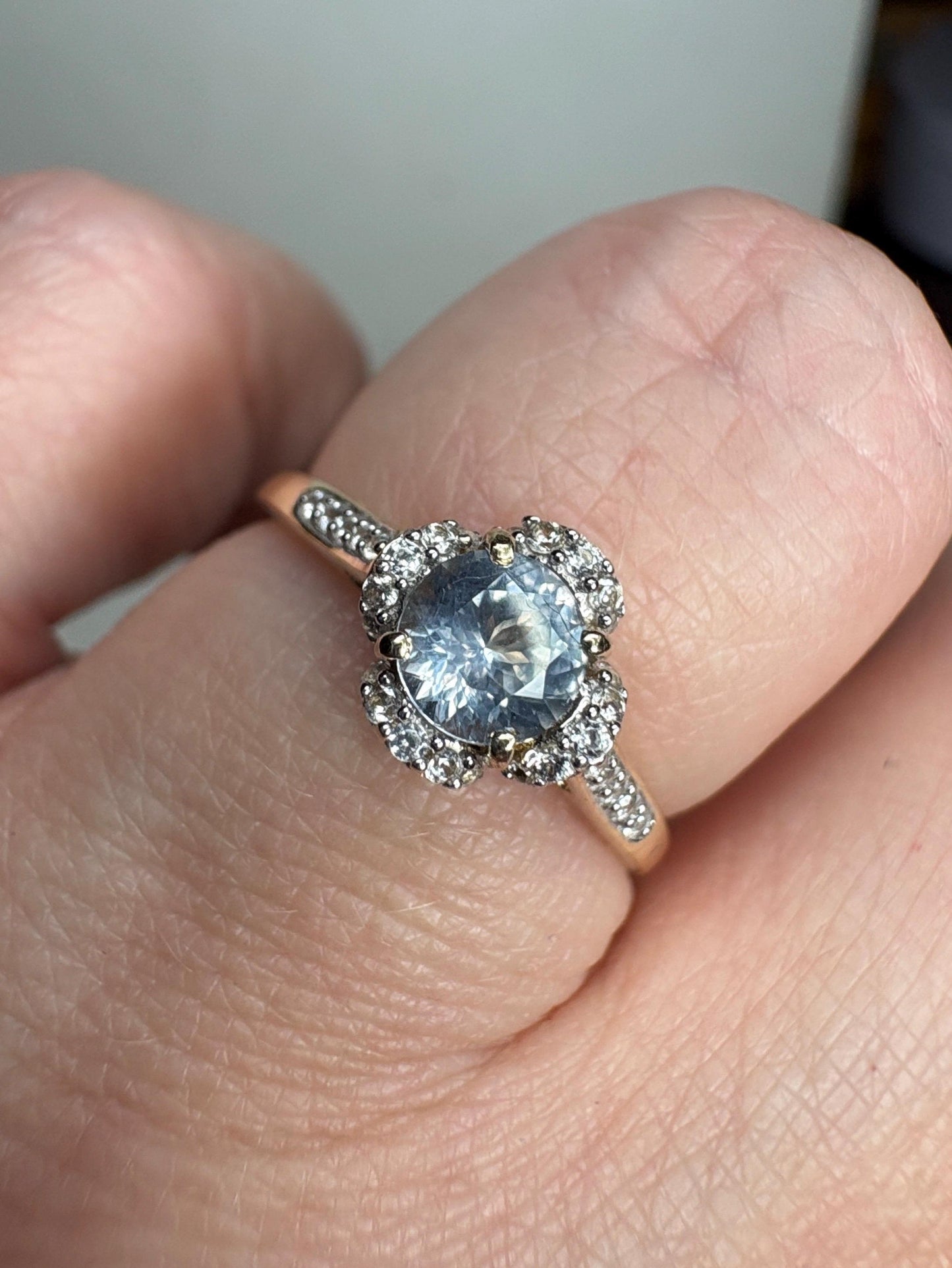 A 9k gold ring with a light blue sapphire and white zircon halo.