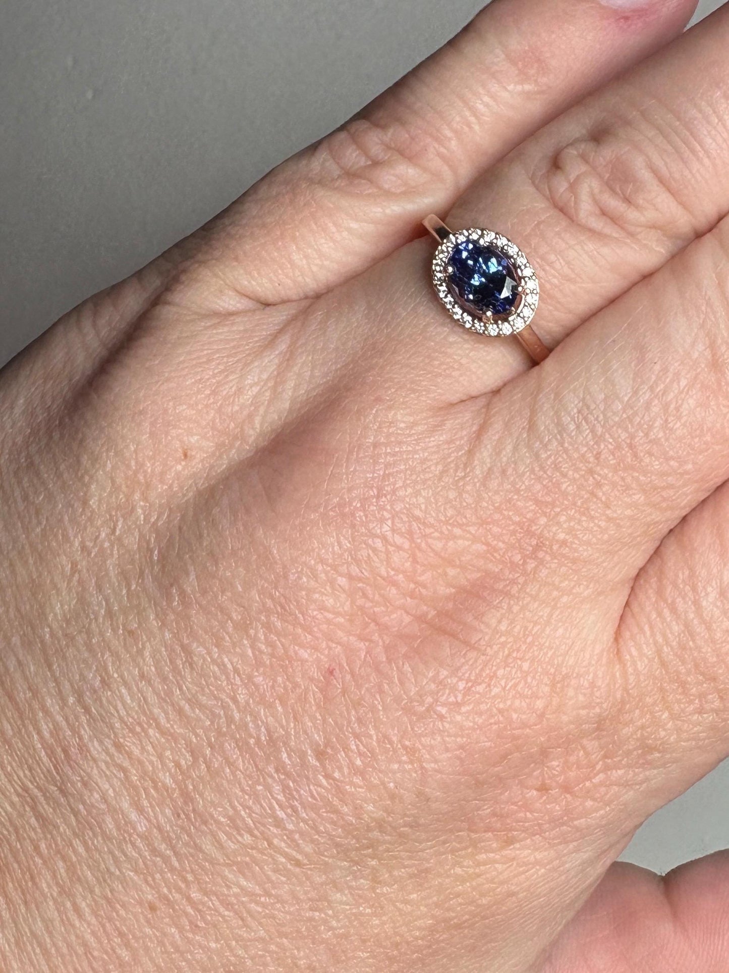 A rose gold ring with an oval tanzanite center stone surrounded by diamonds.