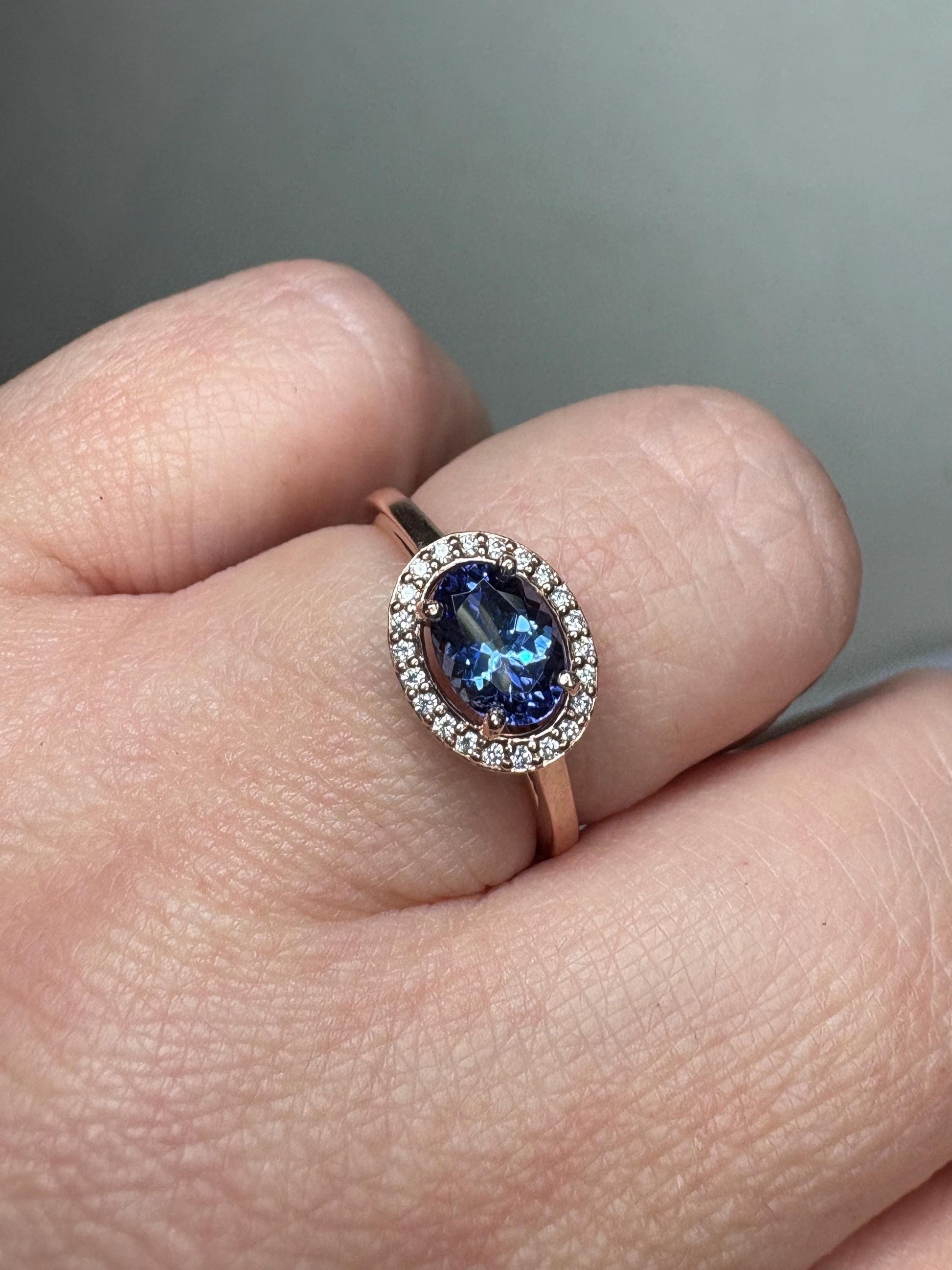 A rose gold ring with an oval tanzanite center stone surrounded by a diamond halo.