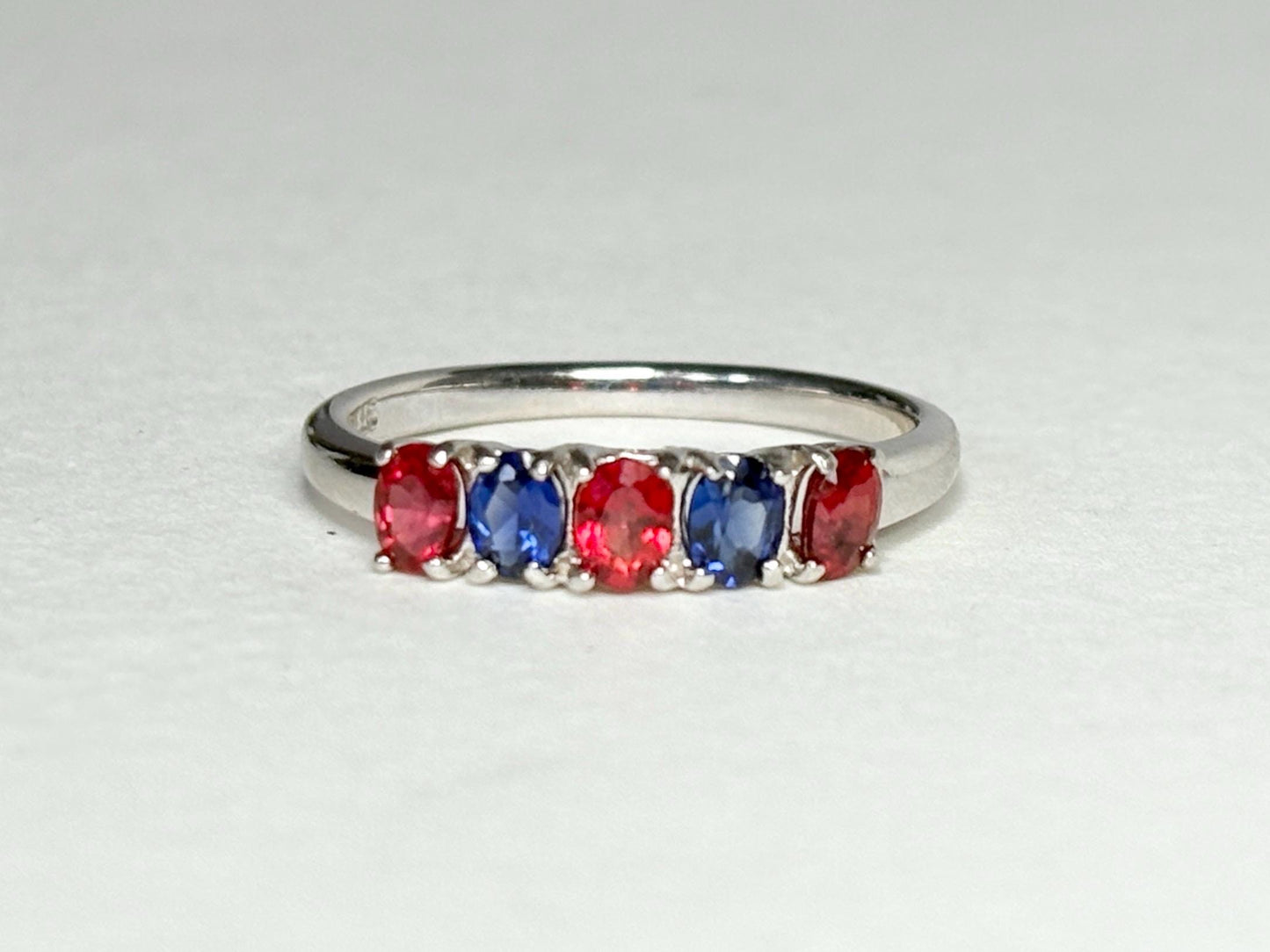 Sterling silver band ring with alternating oval red and blue sapphires.