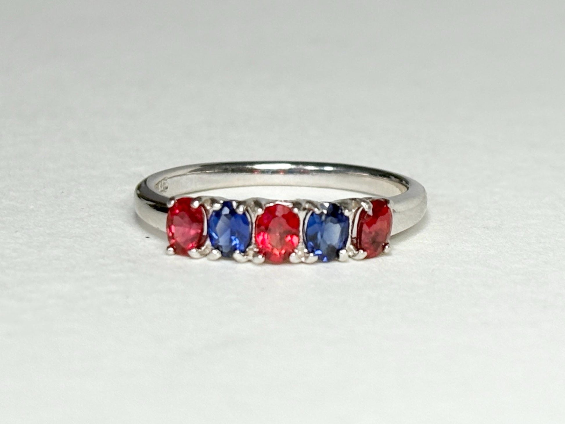 Sterling silver band ring with alternating oval red and blue sapphires.