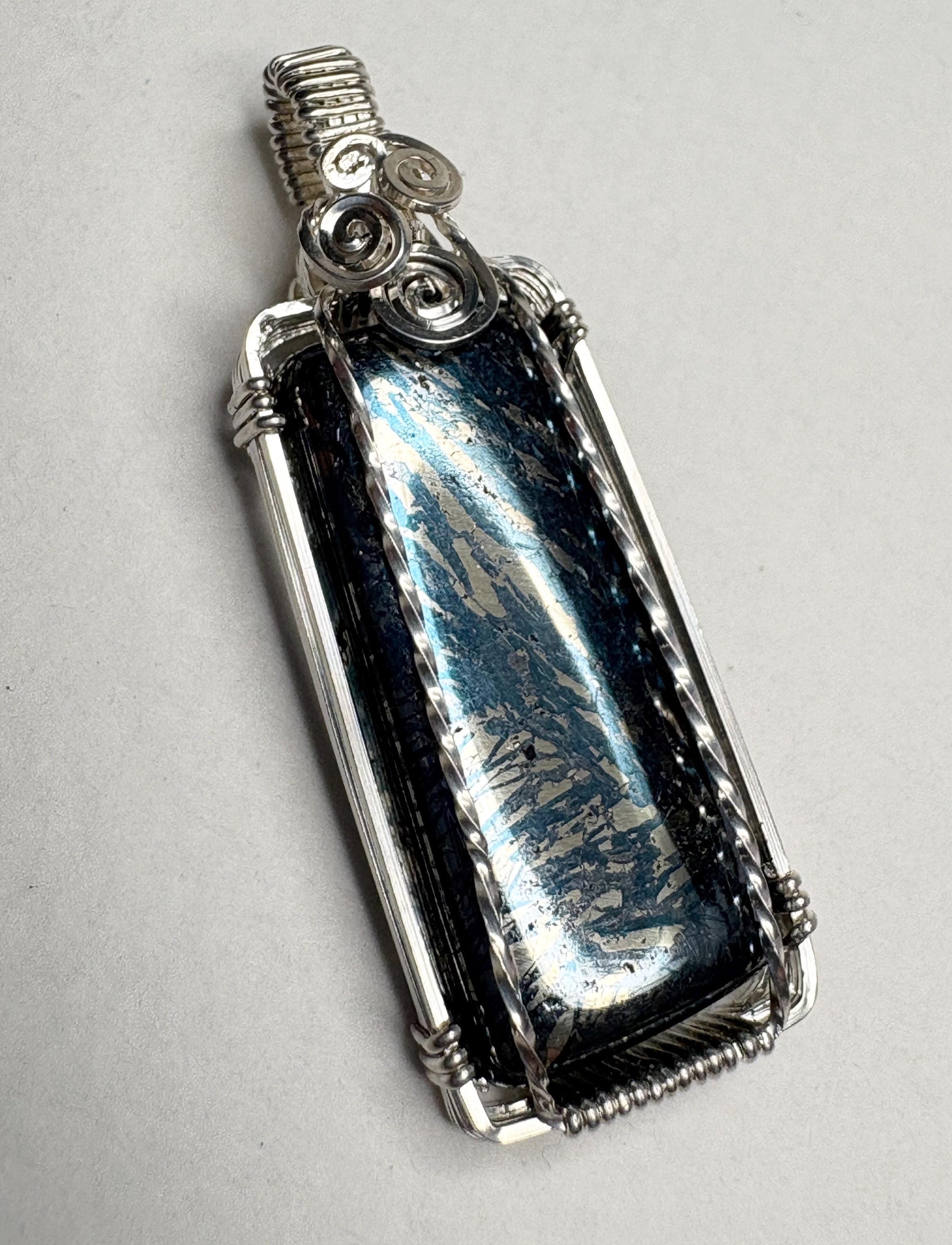 Sterling silver wire-wrapped pendant featuring a rectangular covellite stone with metallic blue and gold patterns.