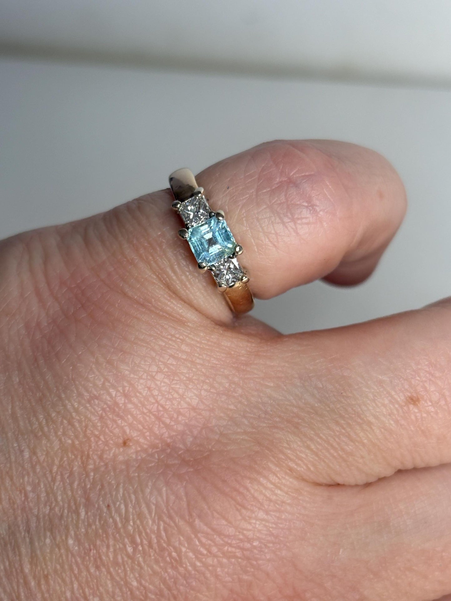 A 14k gold ring with a blue asscher cut tourmaline and two princess cut diamonds.