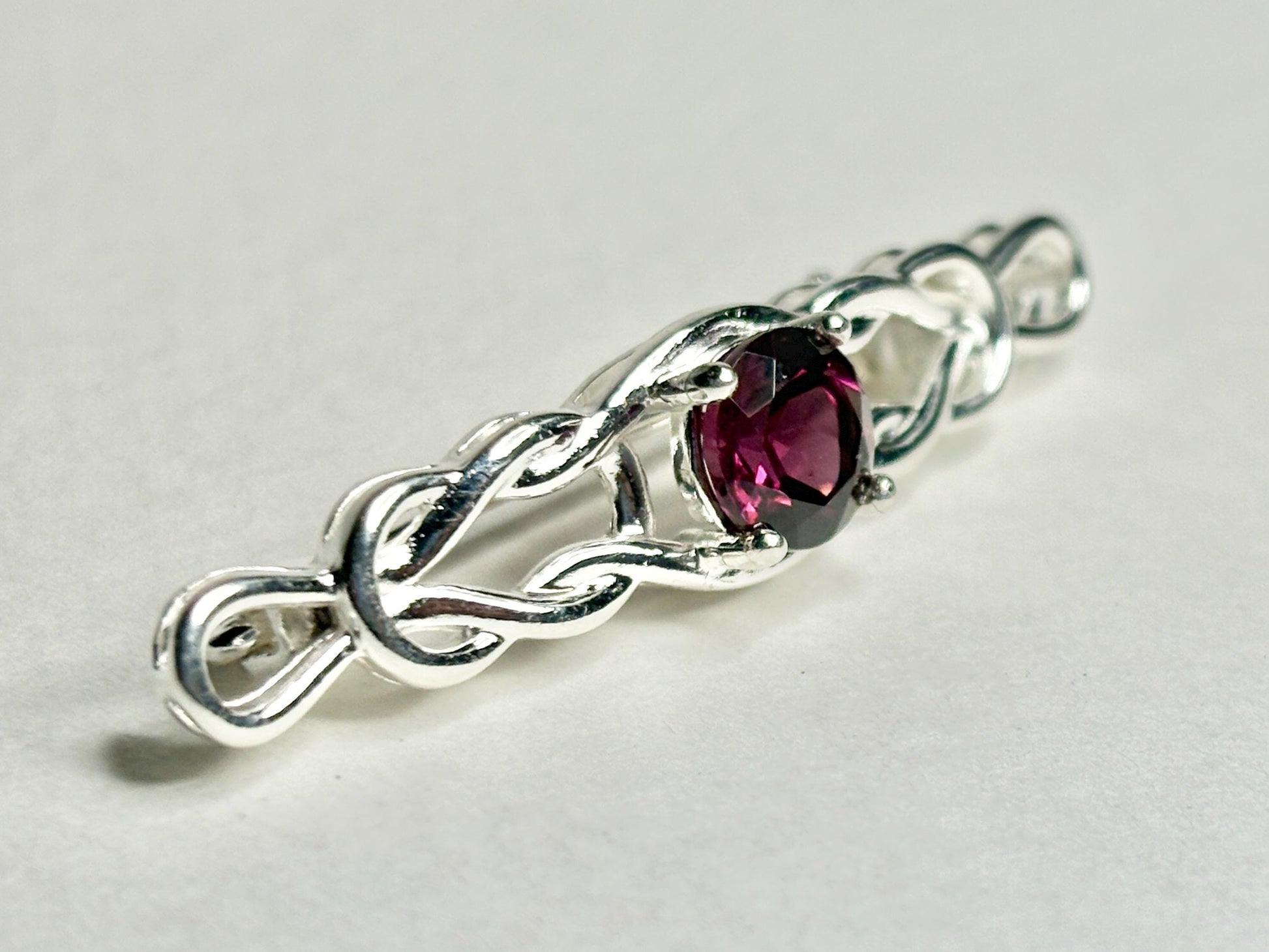 Sterling silver brooch with a Celtic knot design and a rhodolite garnet.