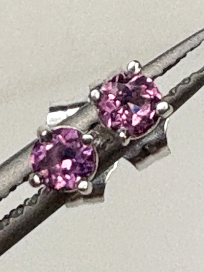 Two small, round rhodolite garnet stud earrings set in 14k white gold.