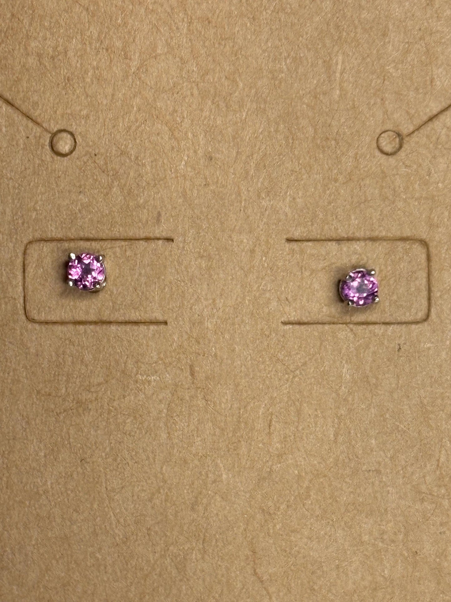 Two small, square-set rhodolite garnet stud earrings with silver settings on a brown background.