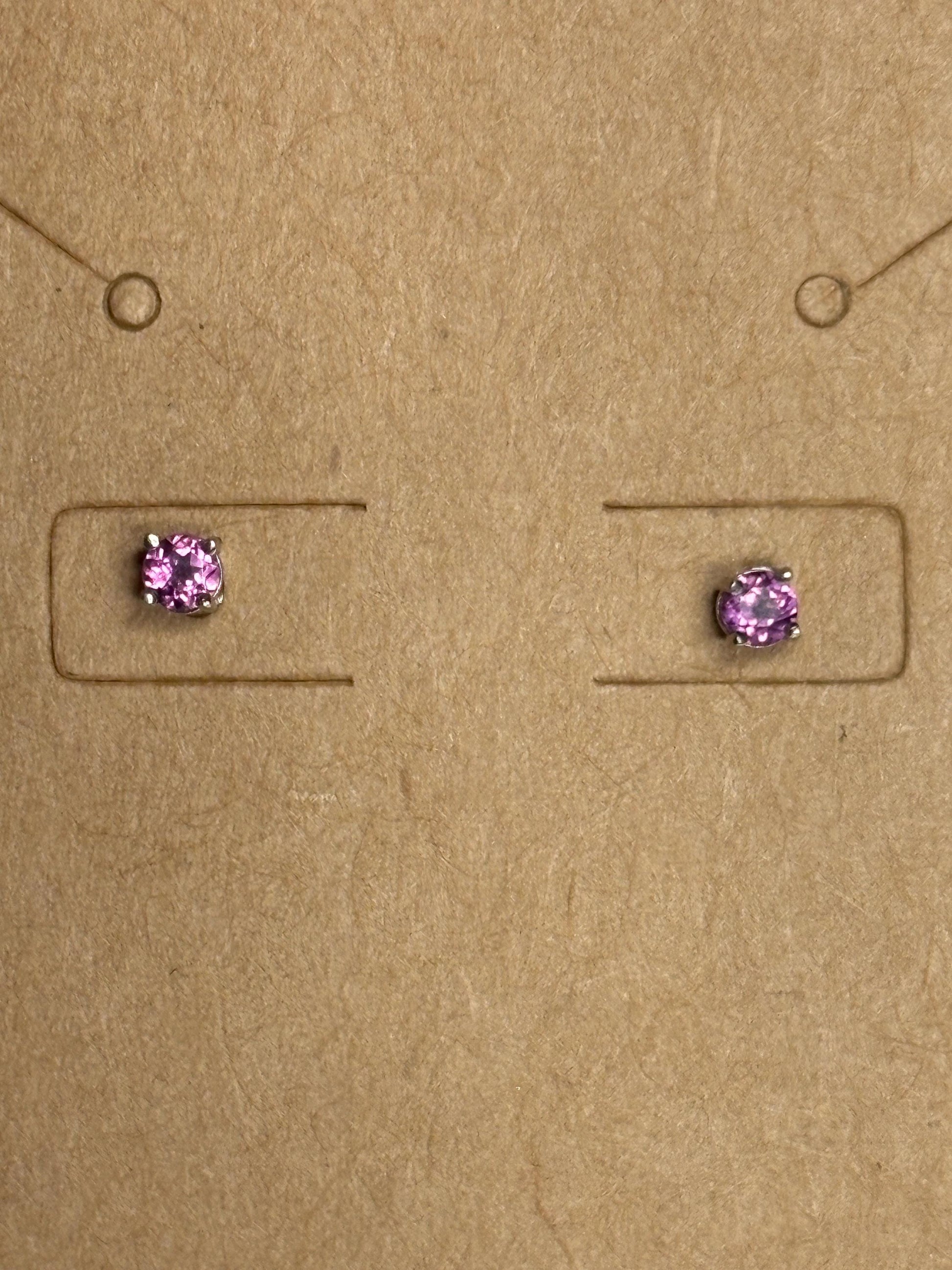 Two small, square-set rhodolite garnet stud earrings with silver settings on a brown background.