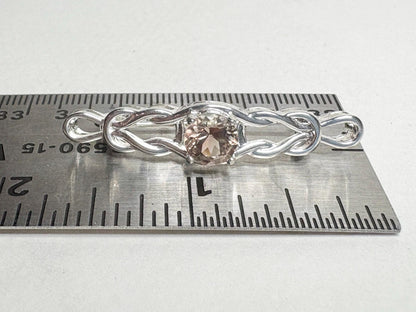 Sterling silver brooch with a Celtic knot design and a light peach Oregon sunstone, shown on a ruler.