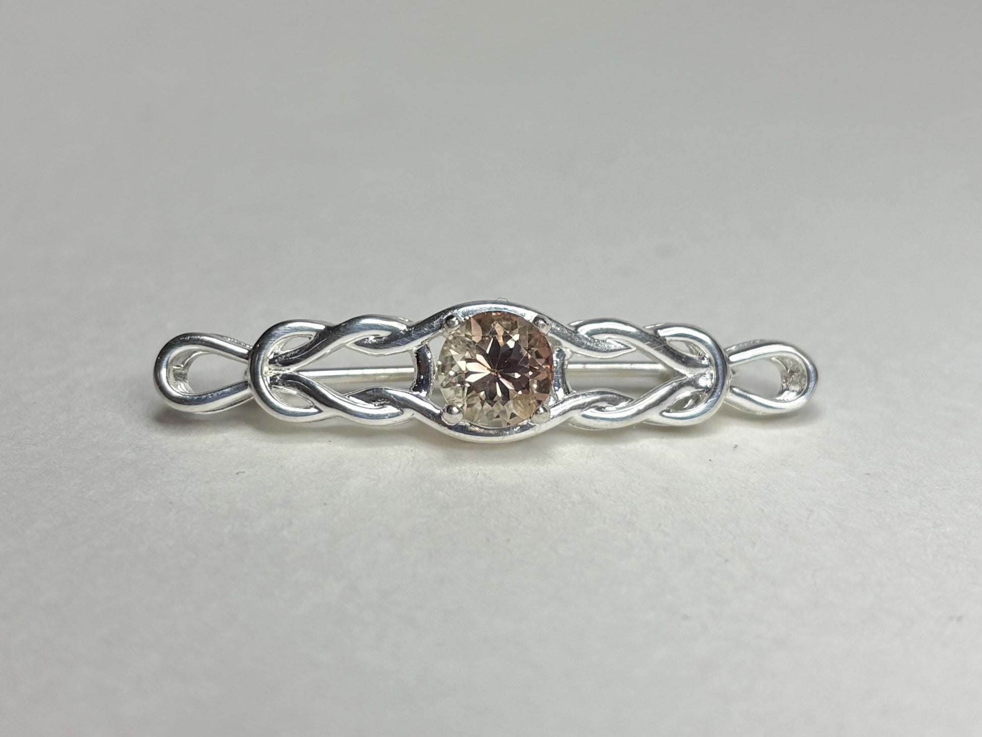 Sterling silver bar brooch with a Celtic knot design and a round light peach Oregon sunstone.