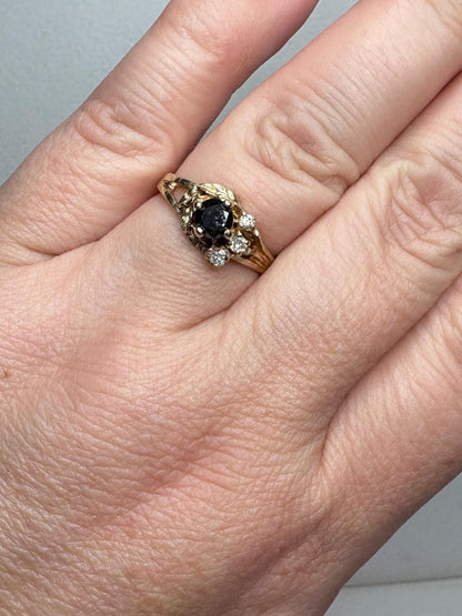 A 10k yellow gold ring with a black diamond center and three white diamonds.