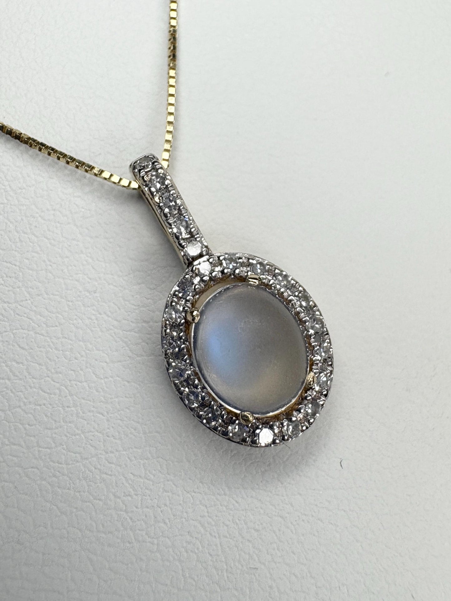Oval moonstone pendant with diamond halo on a gold chain.