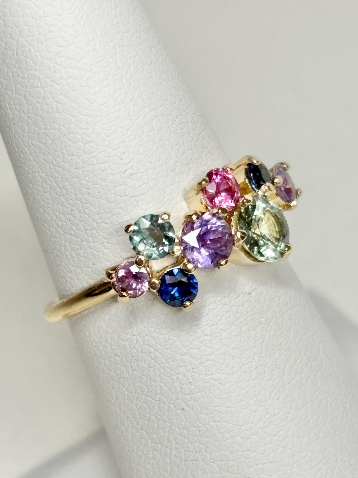 A 10k gold ring featuring a cluster of round multi-colored sapphires.