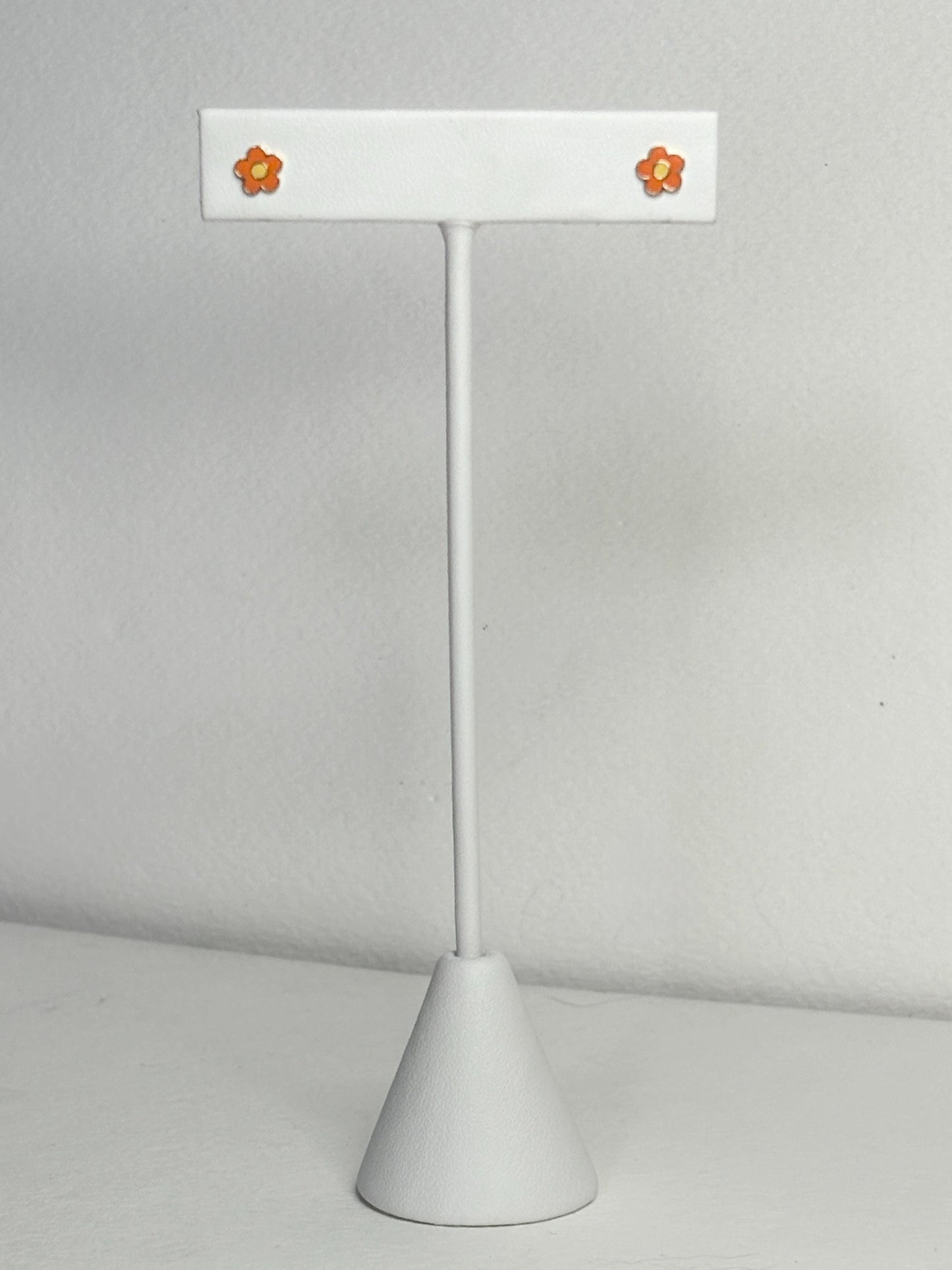 Adorable orange and yellow enamel daisy flower stud earrings on a white display stand.