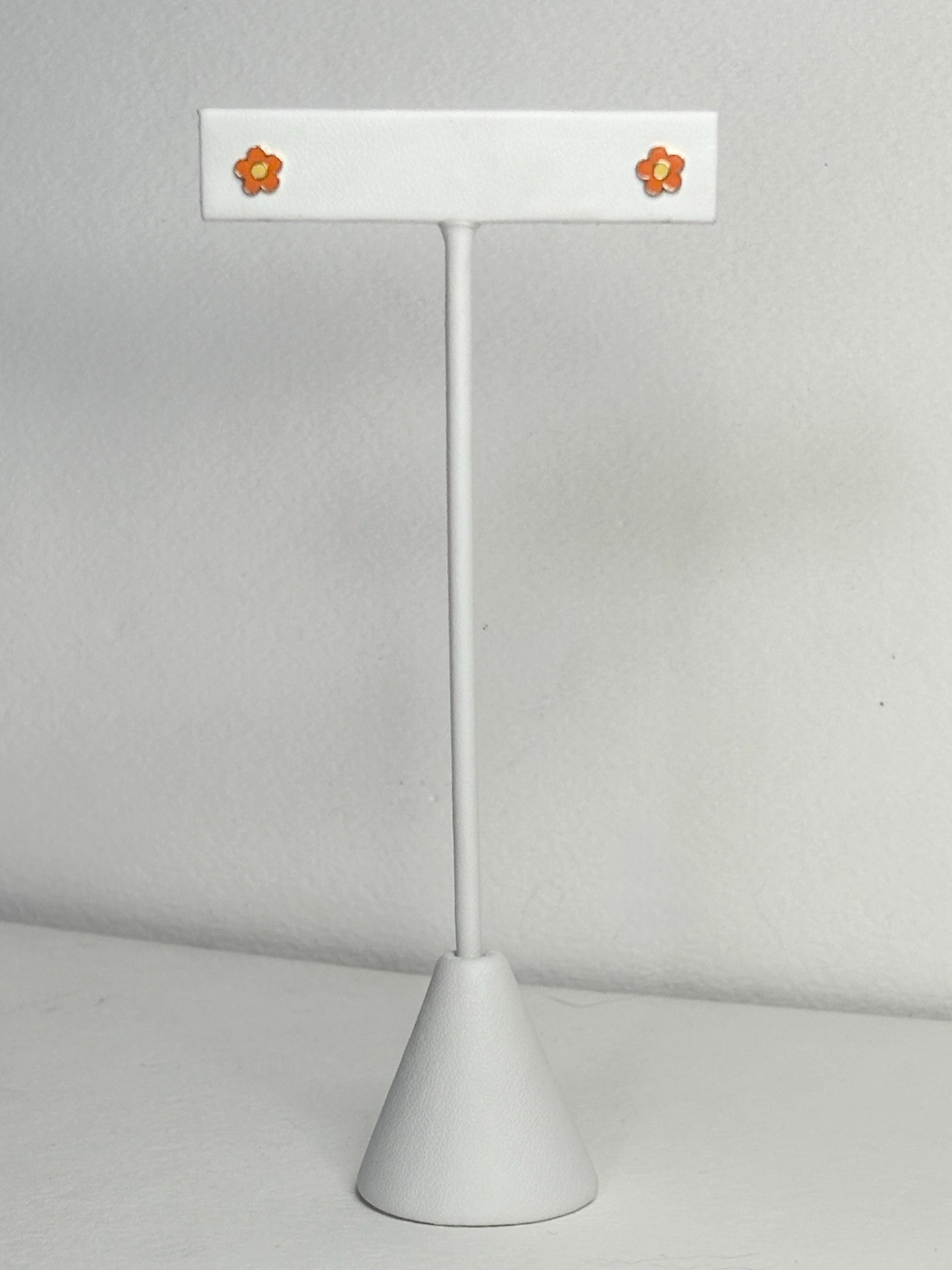 Adorable orange and yellow enamel daisy flower stud earrings on a white display stand.