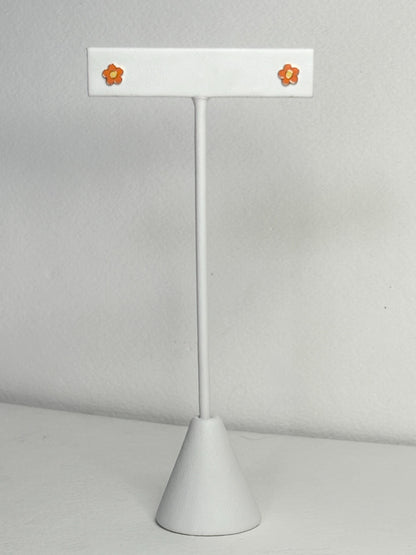 Adorable orange and yellow enamel daisy flower stud earrings on a white display stand.