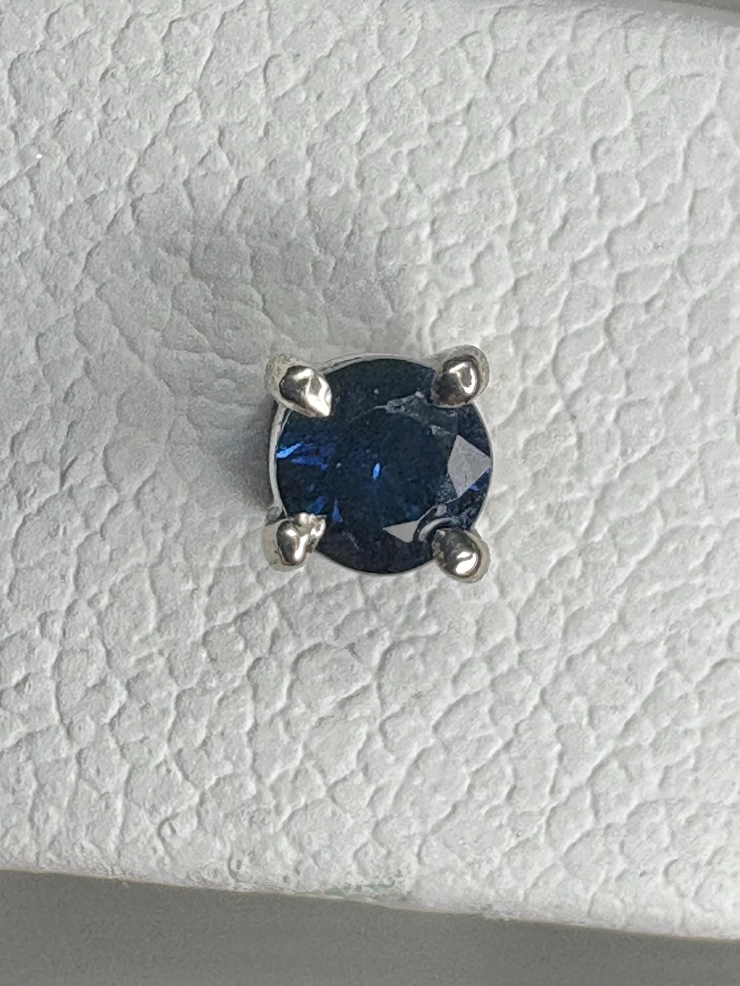 A round, dark blue sapphire is set in a 14k white gold stud earring.