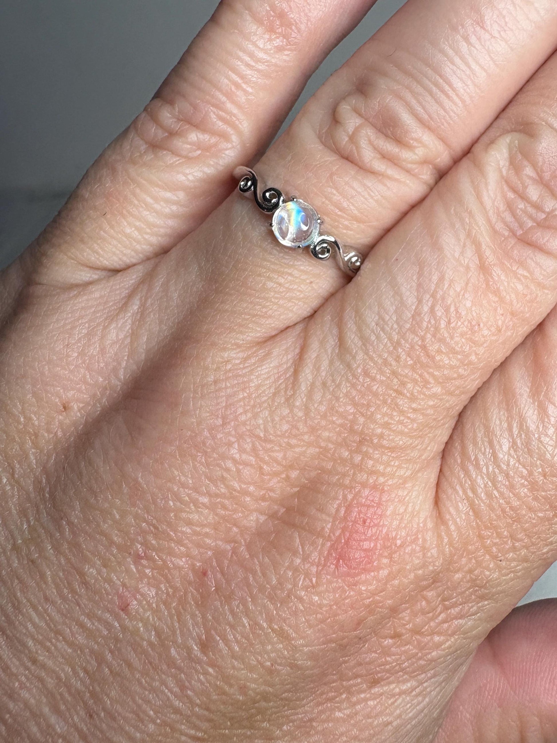 Sterling silver ring with a rainbow moonstone cabochon and swirl design.