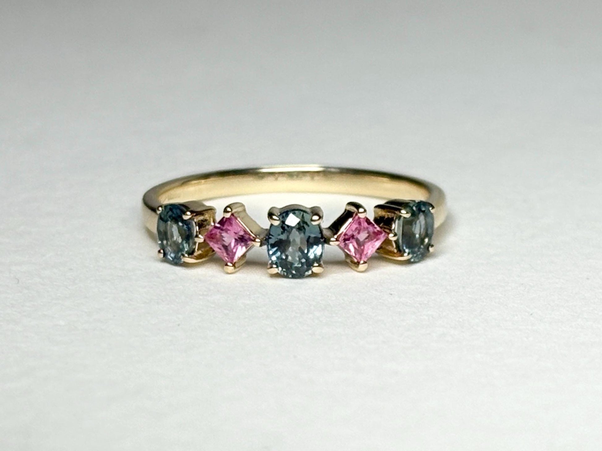 A 9k gold band ring with oval steel blue and square pink sapphires.