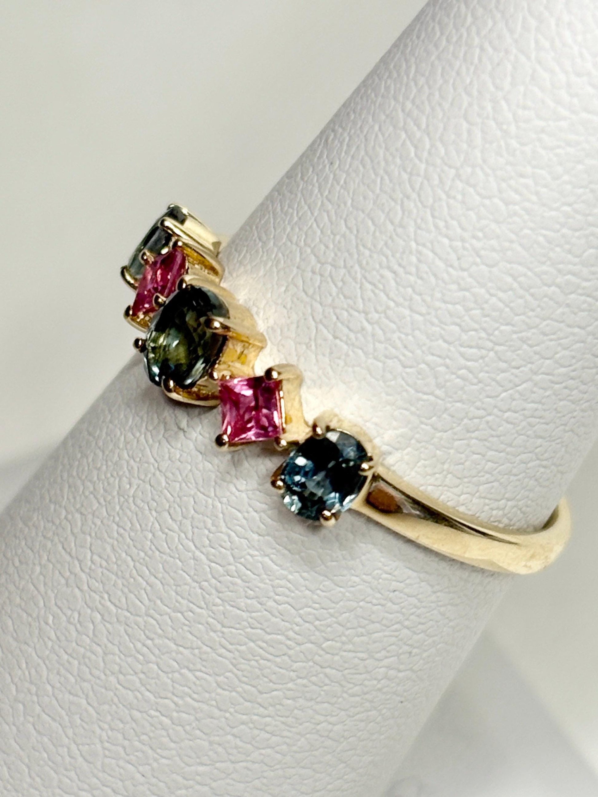 A 9k gold band ring with oval steel blue and square pink sapphires.