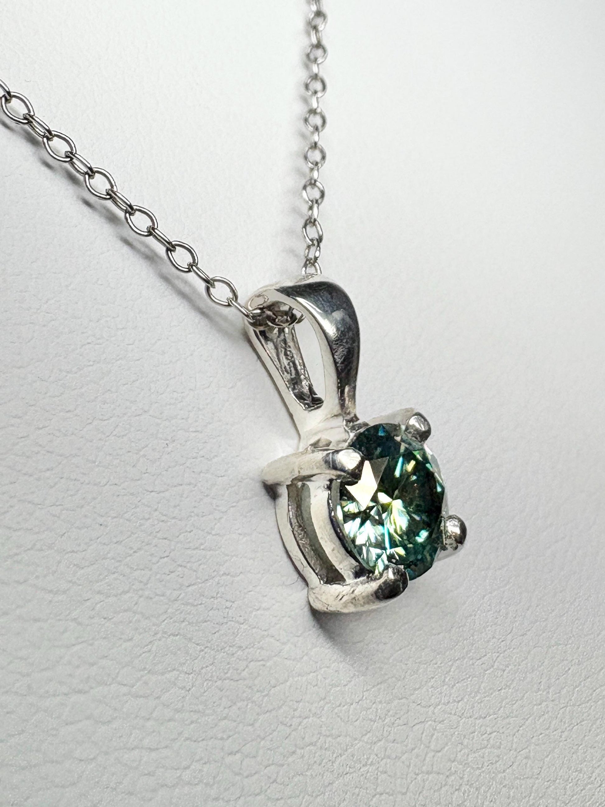 Sterling silver pendant necklace with a teal-green moissanite gemstone.