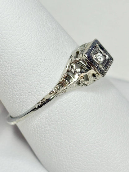 Art Deco 18k gold ring with a diamond chip and filigree details.