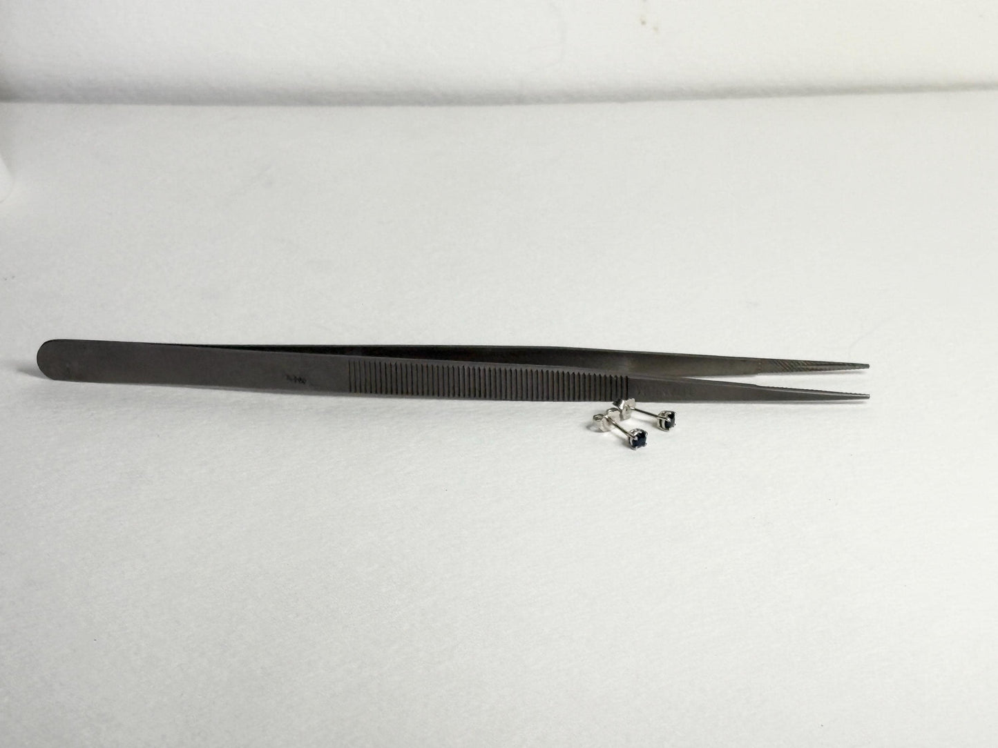 Dark blue sapphire stud earrings in 14k white gold with tweezers.