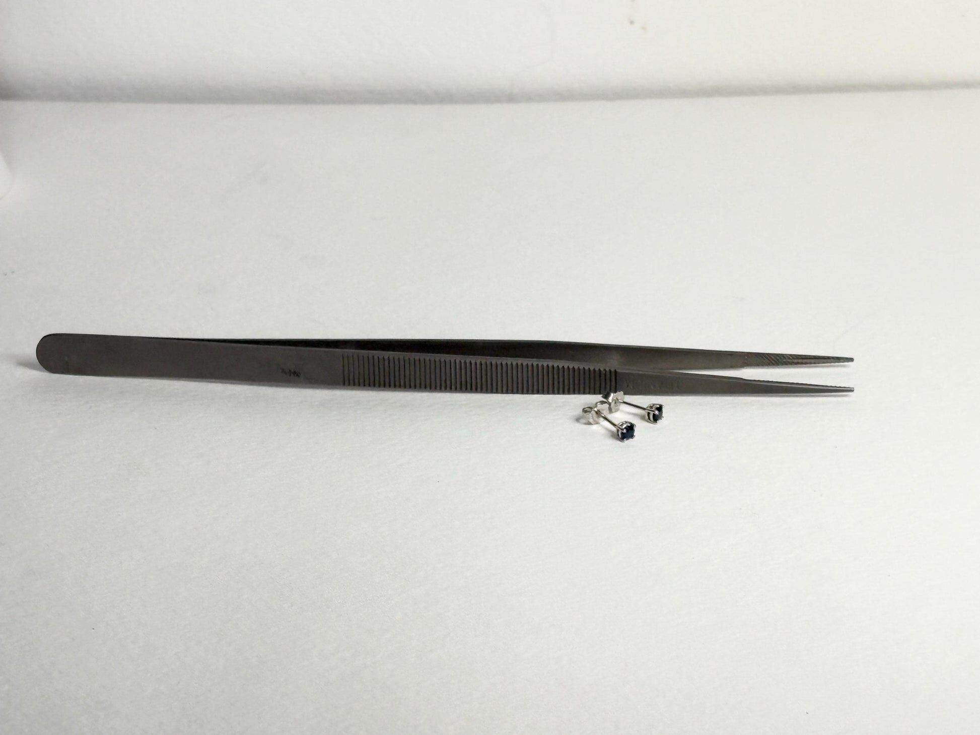 Dark blue sapphire stud earrings in 14k white gold with tweezers.