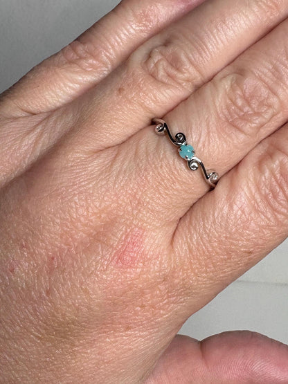 Sterling silver ring with a swirl design and a small blue Paraiba tourmaline.