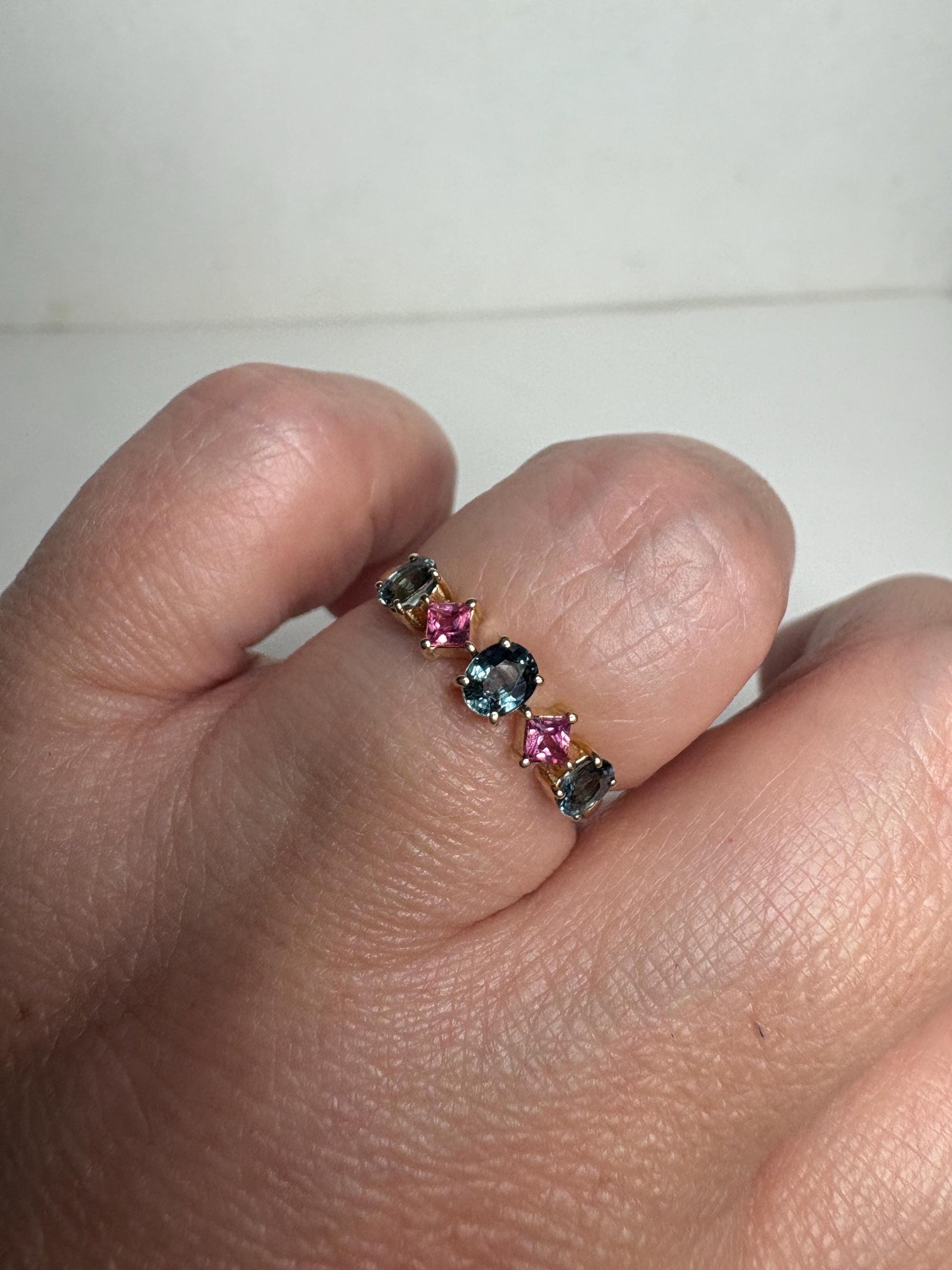 A 9k gold band ring with oval steel blue and square pink sapphires.