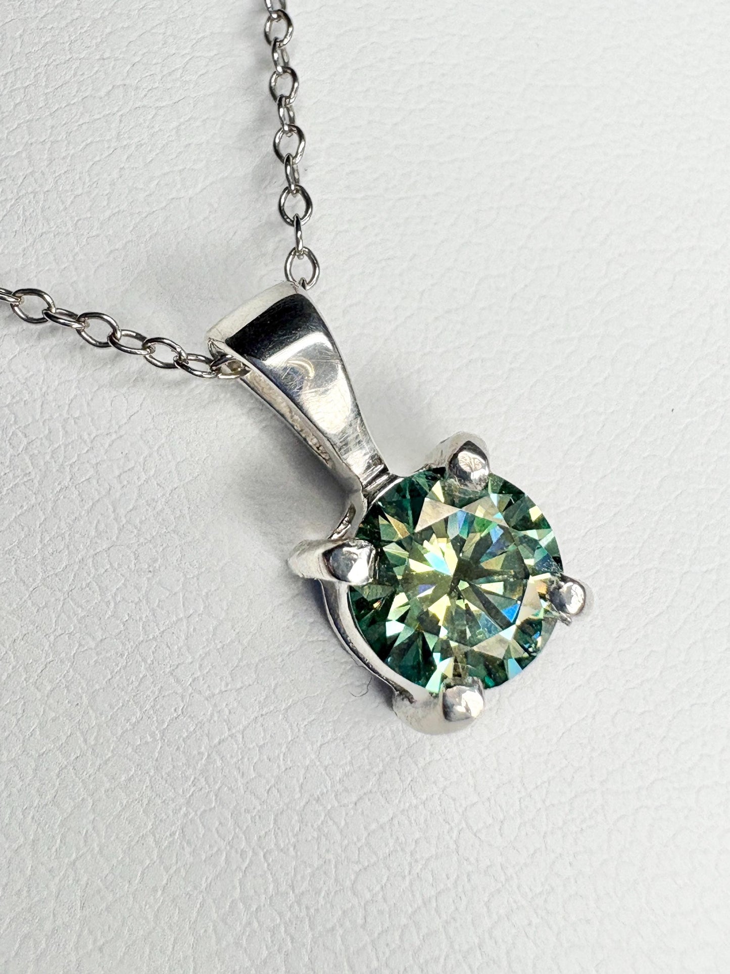 Sterling silver pendant necklace featuring a teal-green moissanite gemstone.