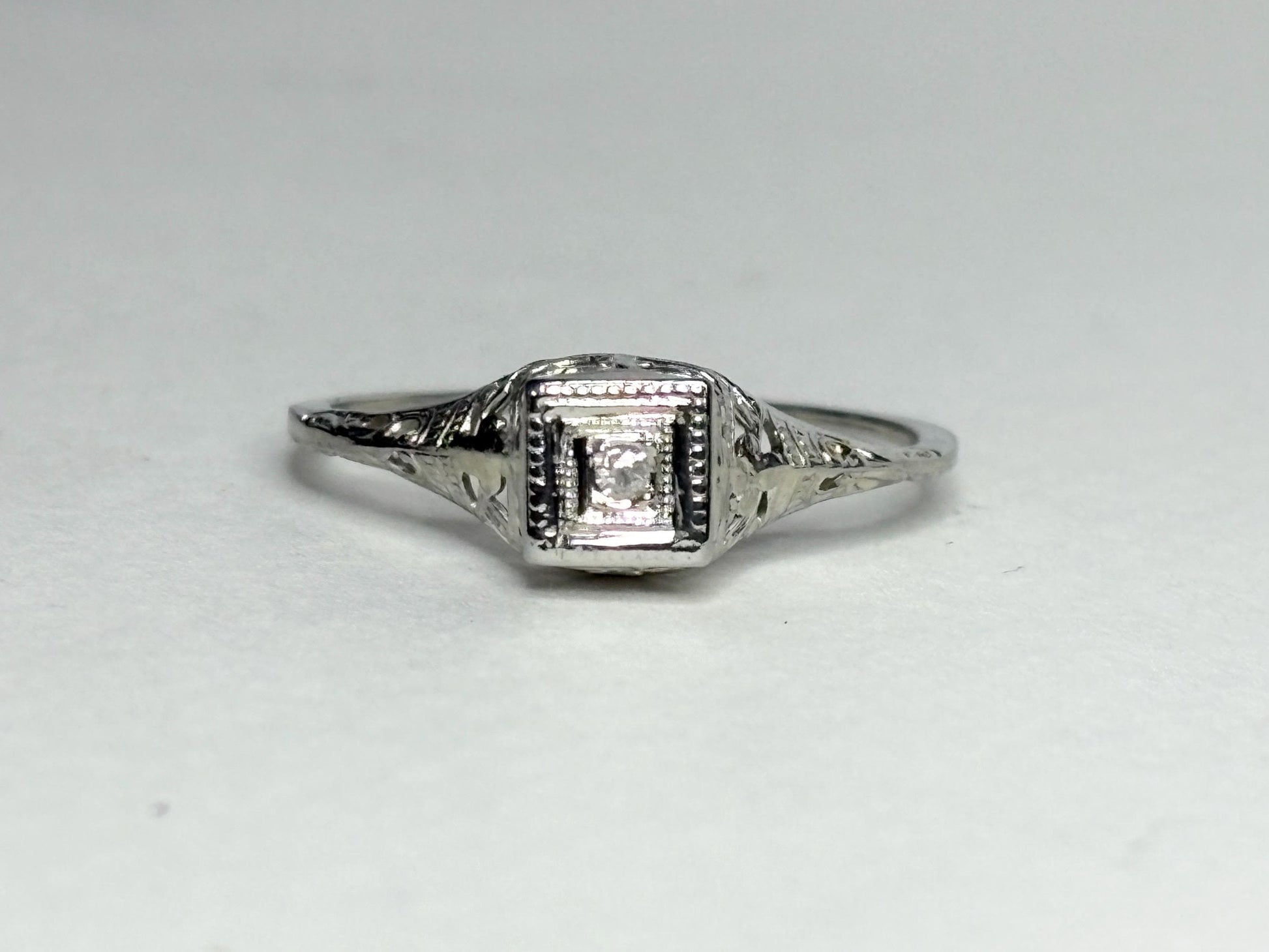 Art Deco 18k gold ring with a diamond chip and filigree details.