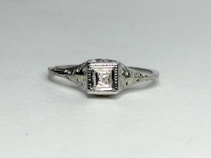 Art Deco 18k gold ring with a diamond chip and filigree details.