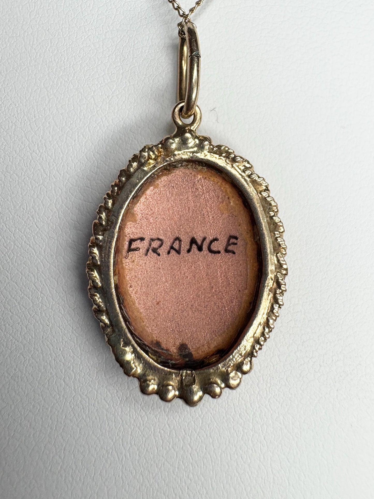 Oval gold pendant with "France" written on a pink background.