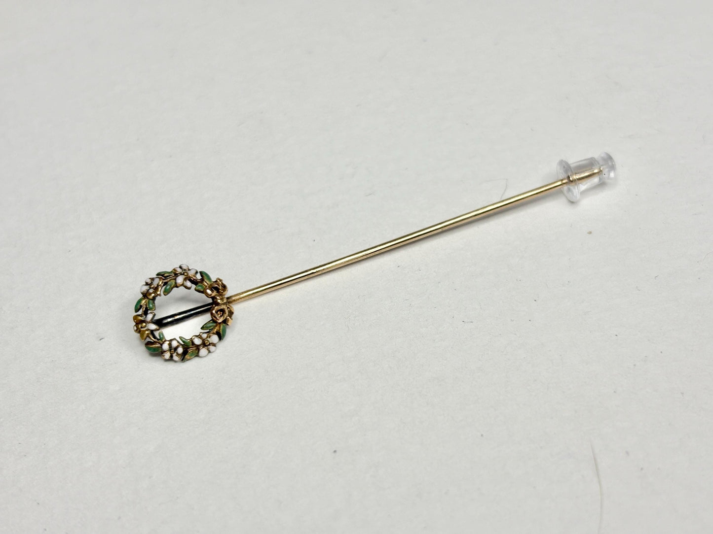 A 14k gold stick pin with a floral wreath design featuring enameled flowers and leaves.
