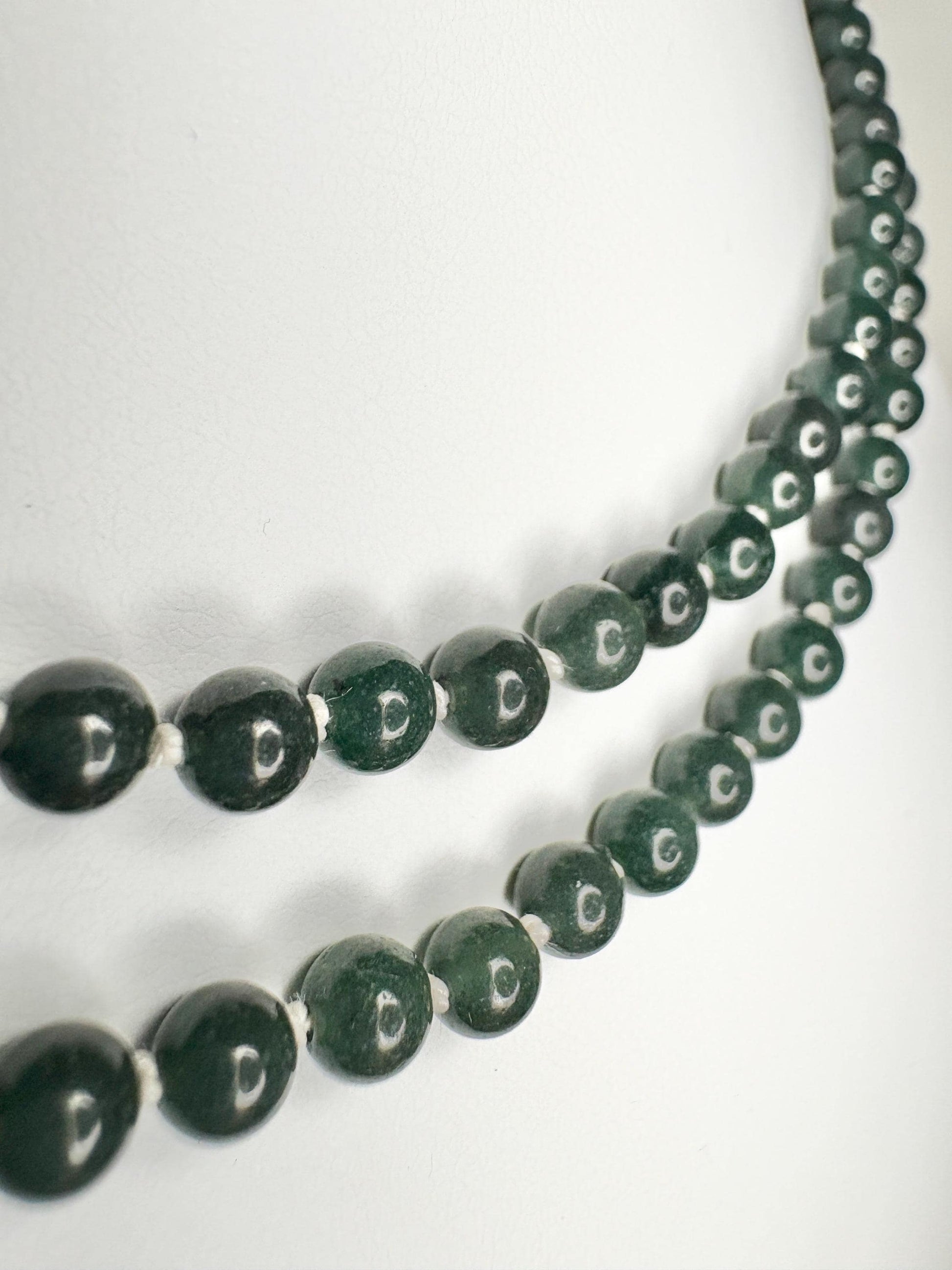 Teal jadeite jade beads on a white silk cord with a sterling silver clasp.