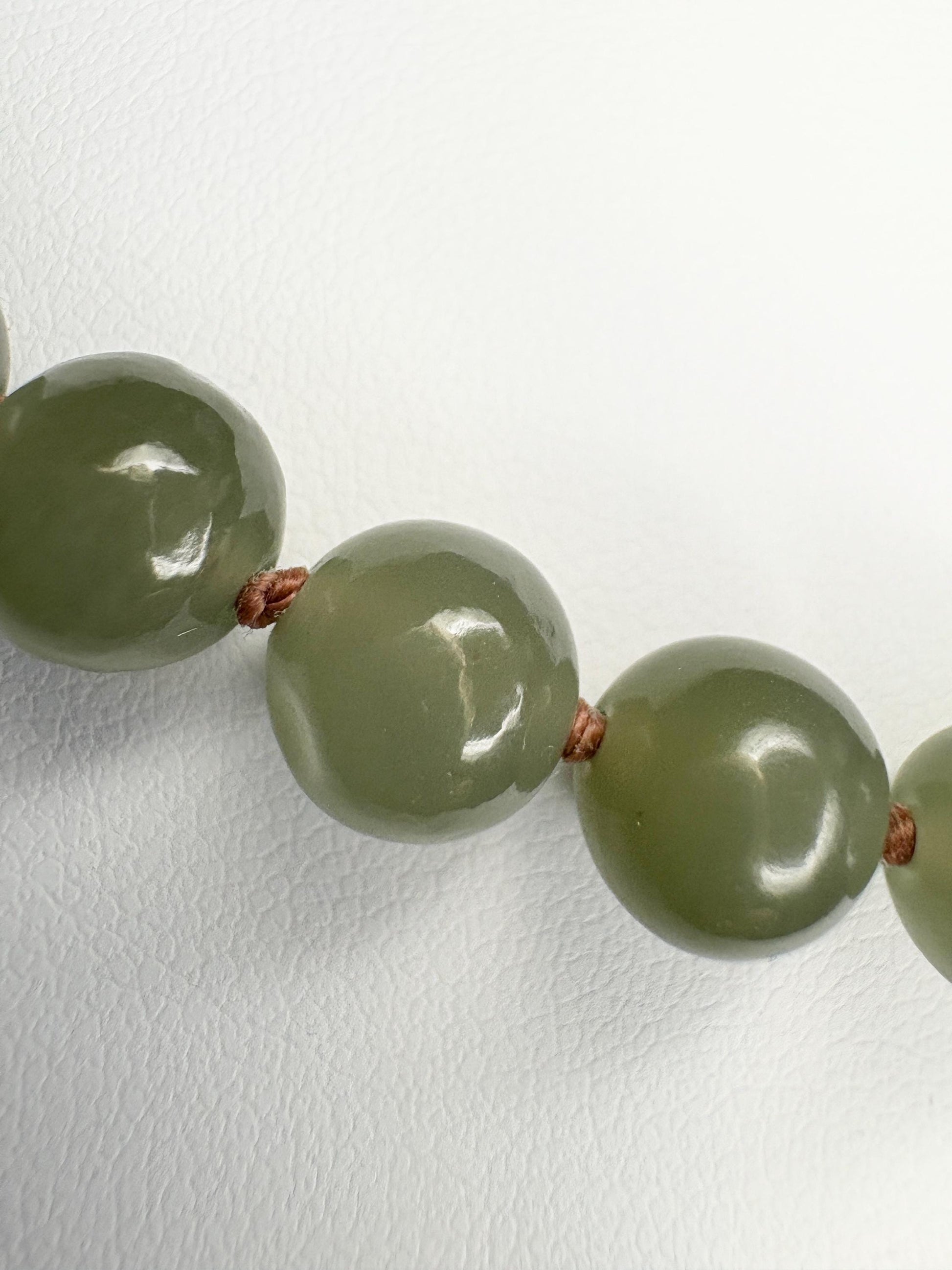 Nephrite Hetian jade beads knotted on a brown cord with a sterling silver toggle clasp.