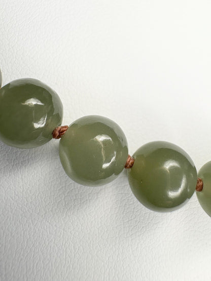 Nephrite Hetian jade beads knotted on a brown cord with a sterling silver toggle clasp.