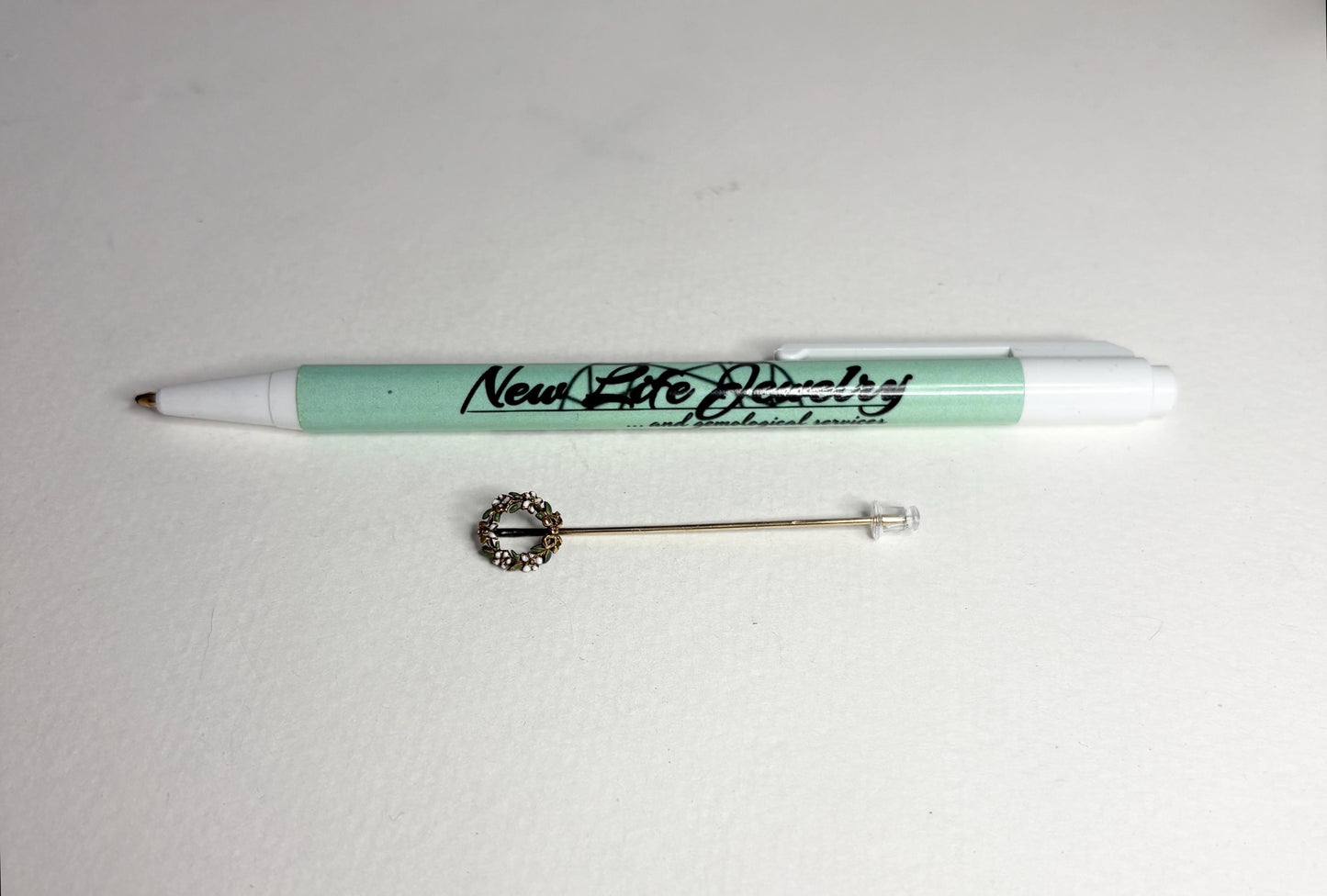 A 14k gold stick pin featuring a floral wreath with enameled leaves and flowers.