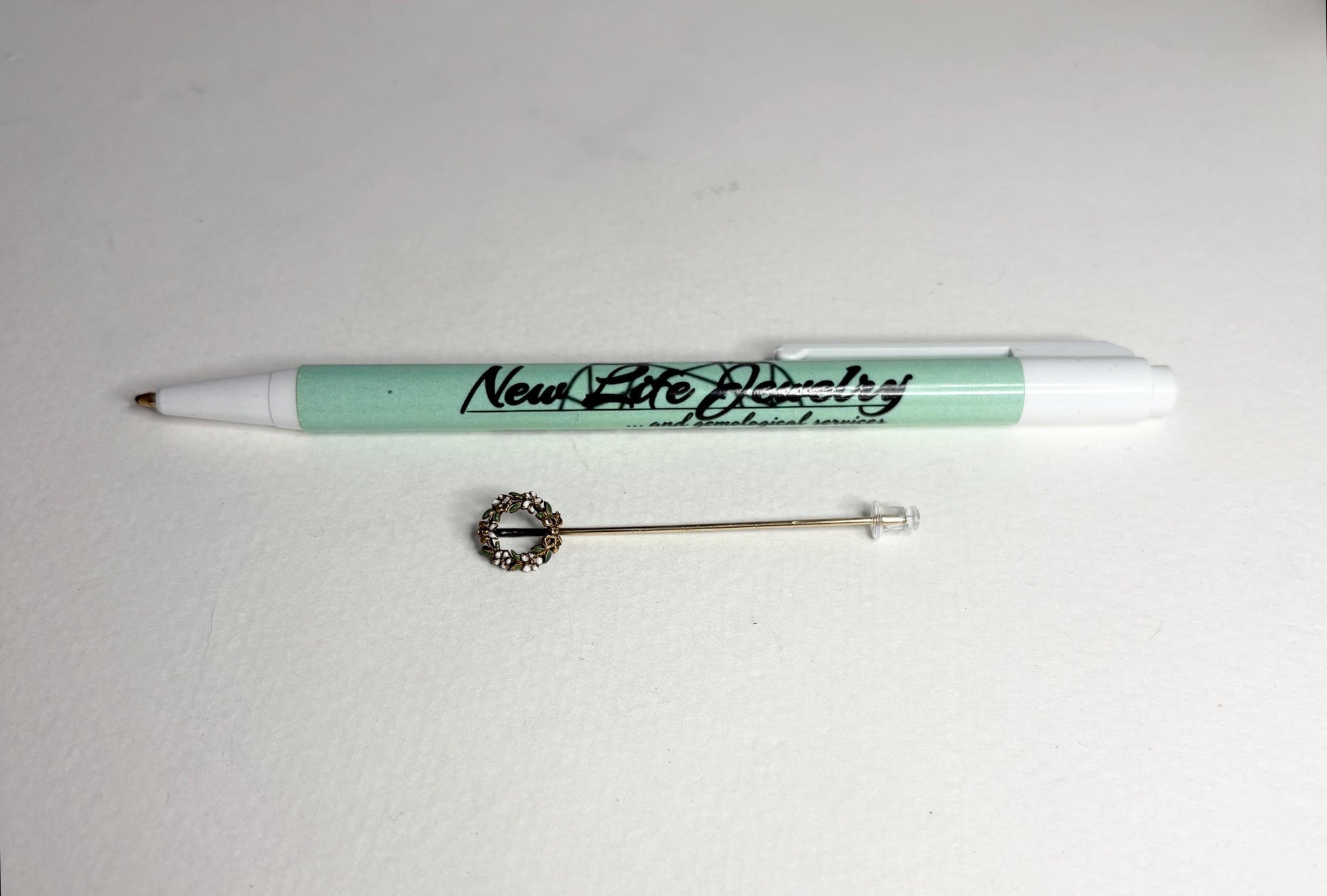 A 14k gold stick pin featuring a floral wreath with enameled leaves and flowers.