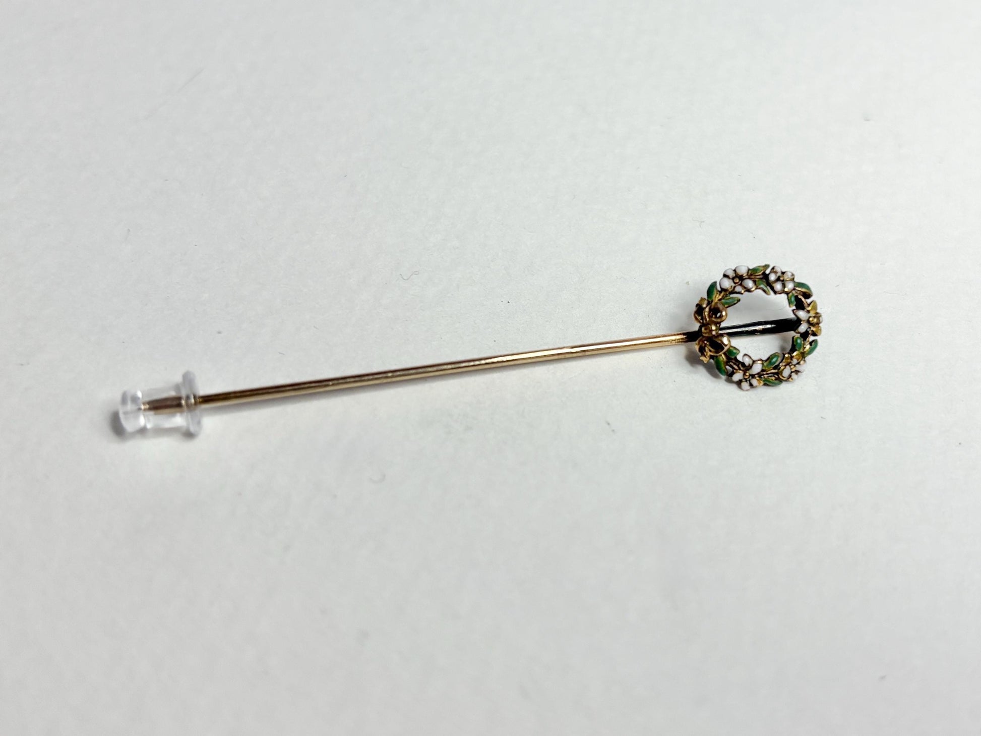 A 14k gold stick pin with an enameled floral wreath.