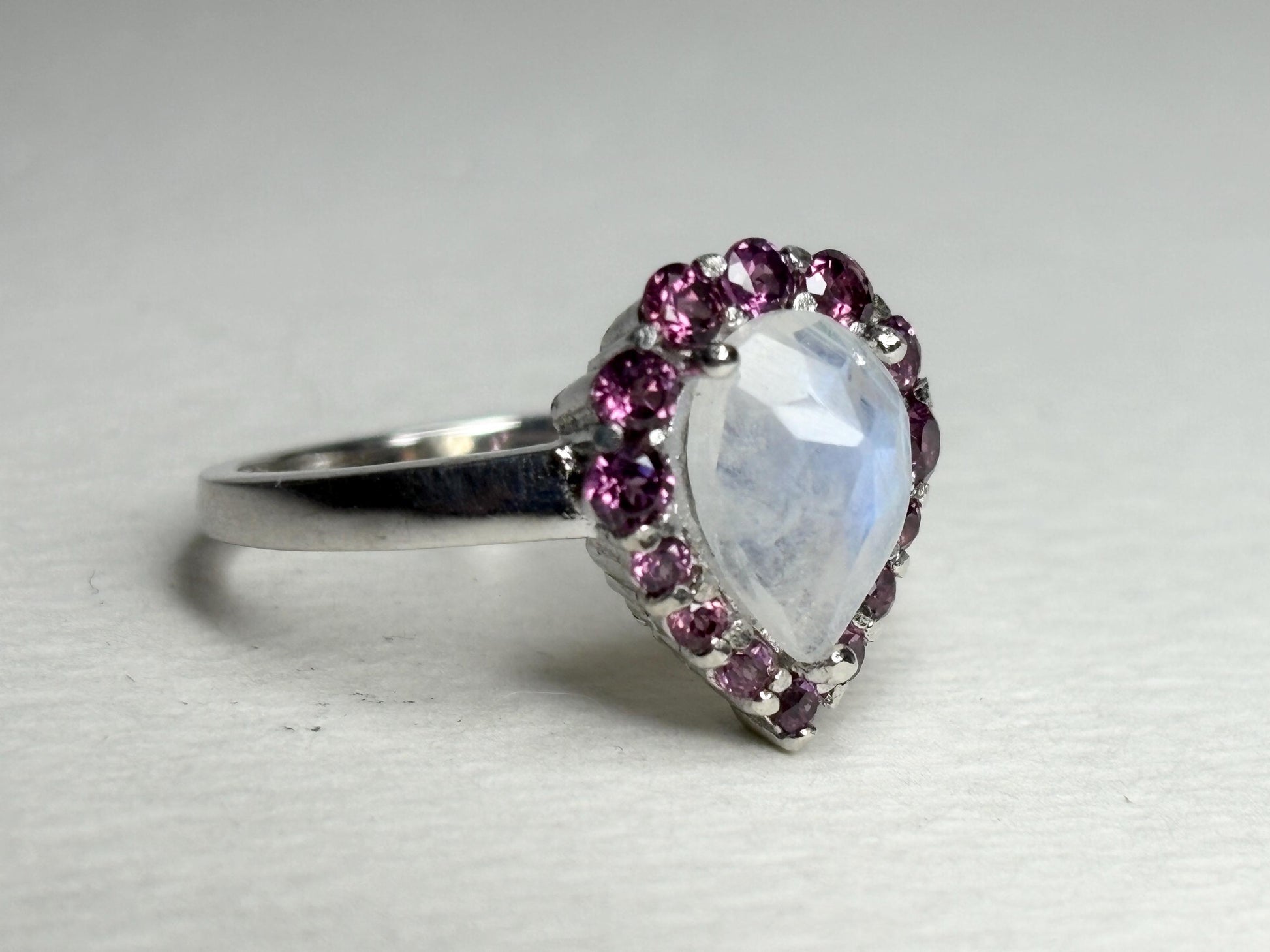 Sterling silver ring with pear-shaped rainbow moonstone and rhodolite garnet halo.