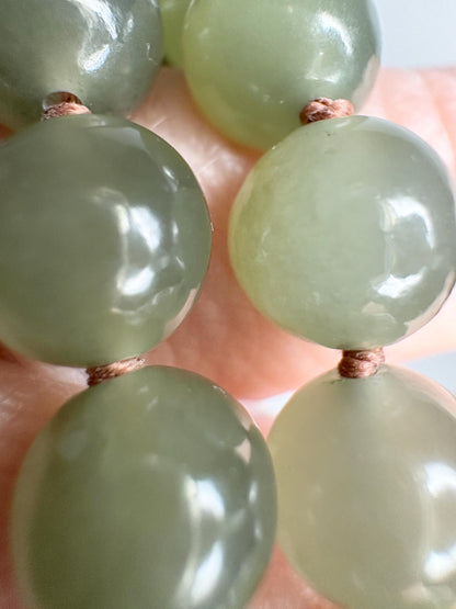 A bracelet of green nephrite jade beads knotted on brown cord.