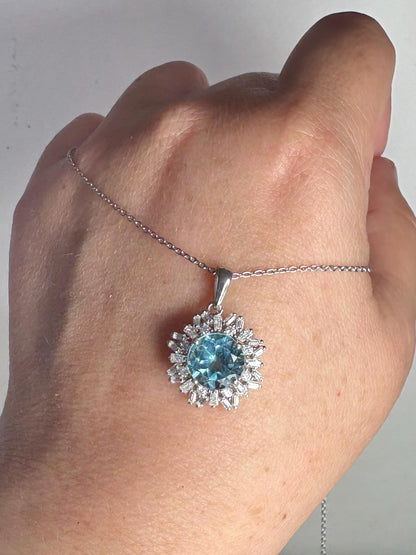 Sterling silver pendant necklace with a blue topaz center and moissanite halo.