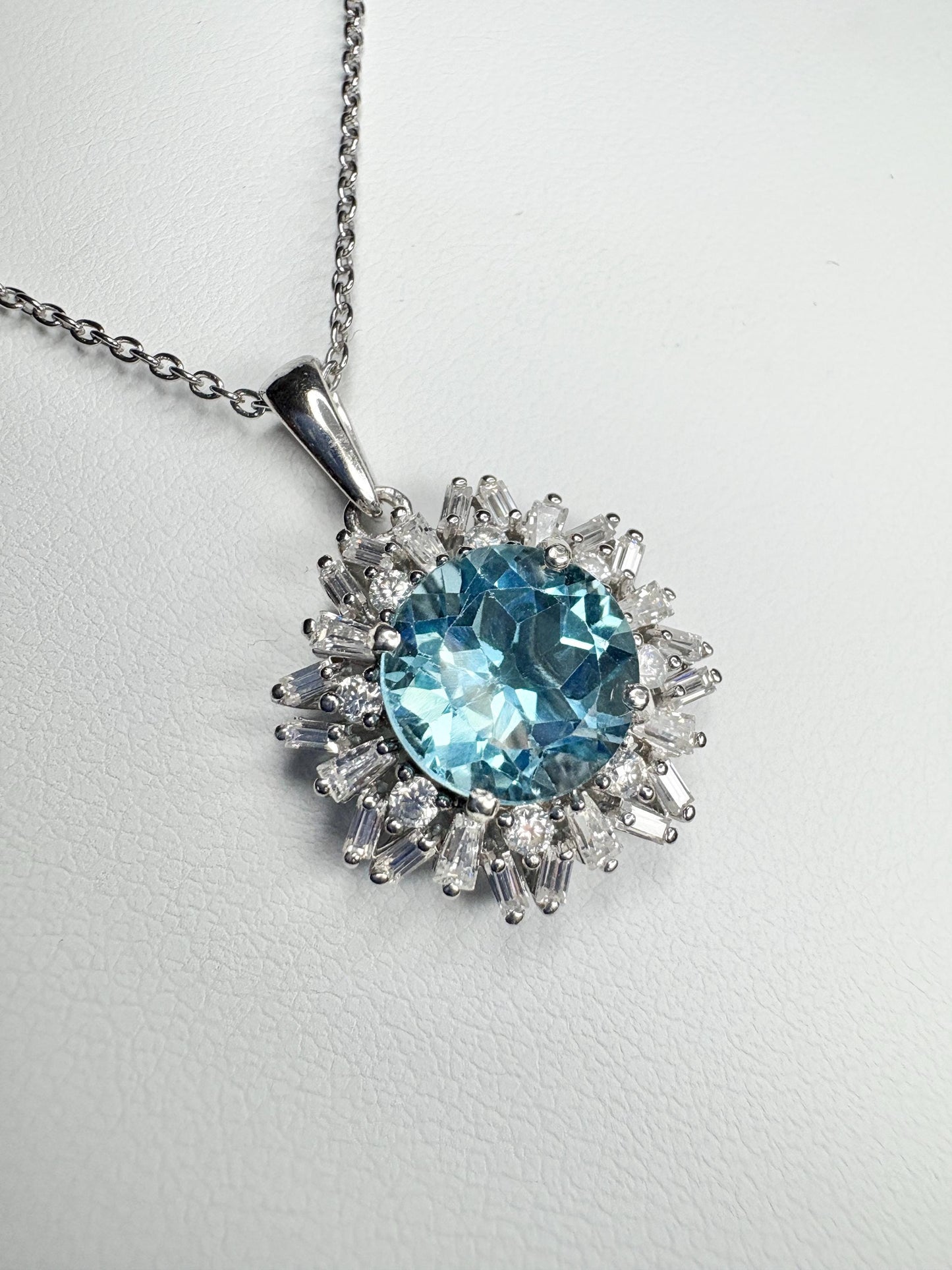 Sterling silver pendant necklace with a blue topaz center and moissanite halo.